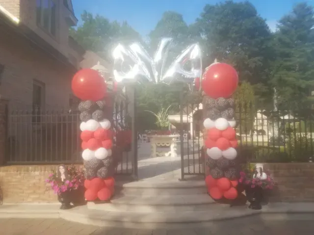 A row of red , white and gray balloons are lined up in front of a gate.