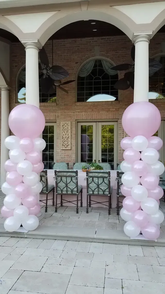 Pink and white balloons are stacked on top of each other on a porch.