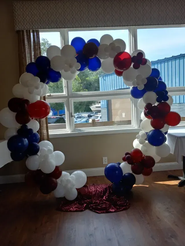 A room decorated with red , white and blue balloons in front of a window.