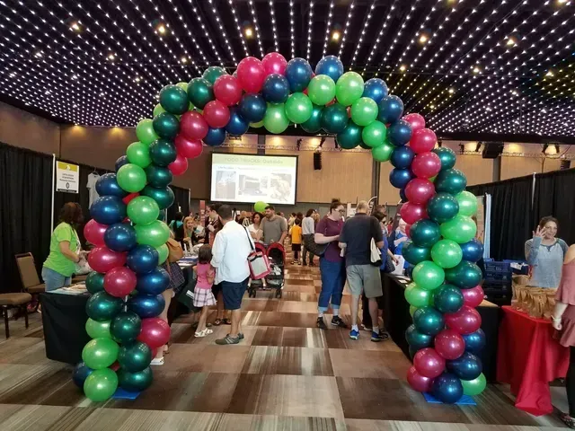 A group of people are standing under a balloon arch in a room.