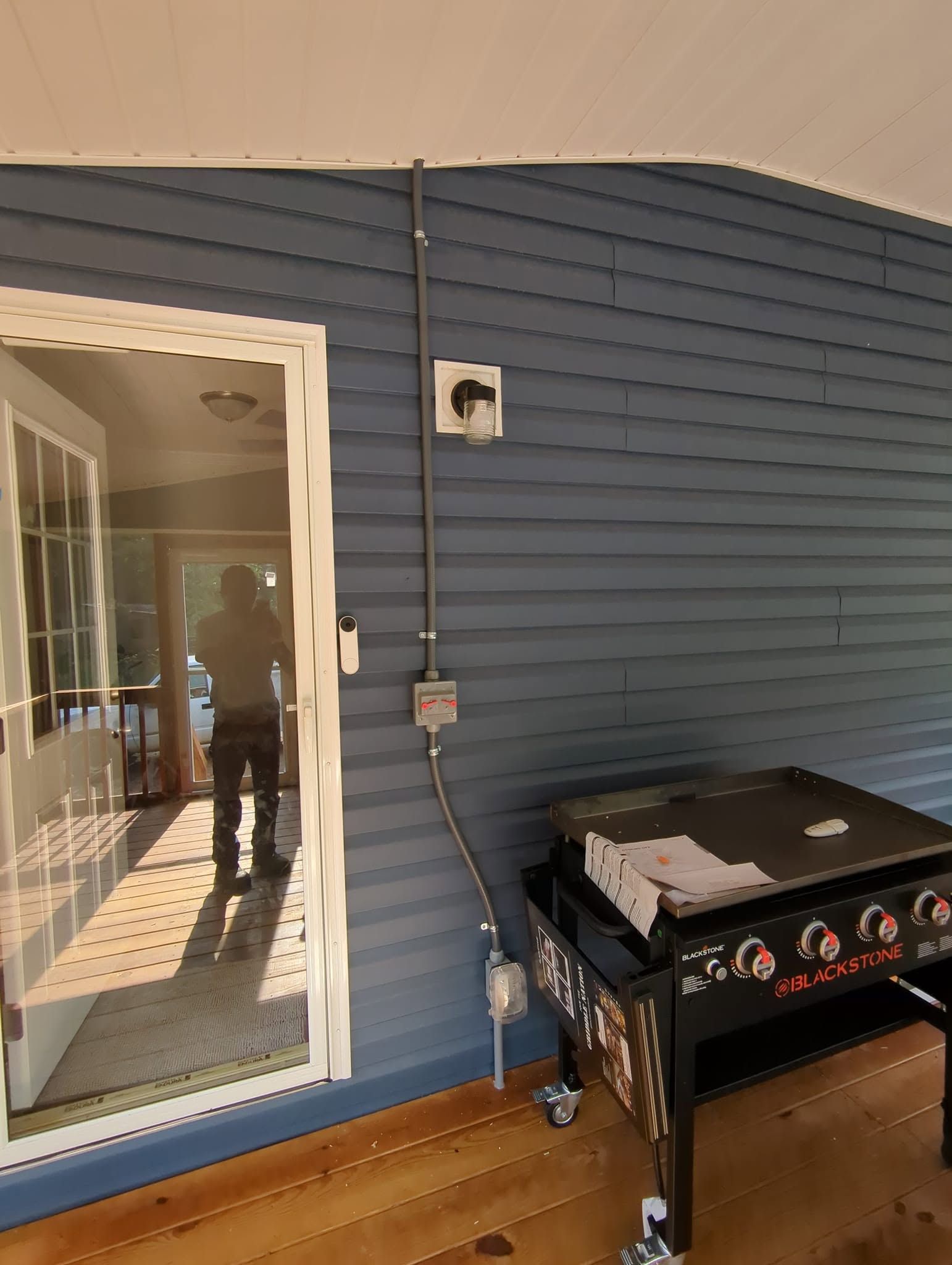 Blue siding wall beside a glass door, with a black outdoor grill and small utility box on a wooden deck.