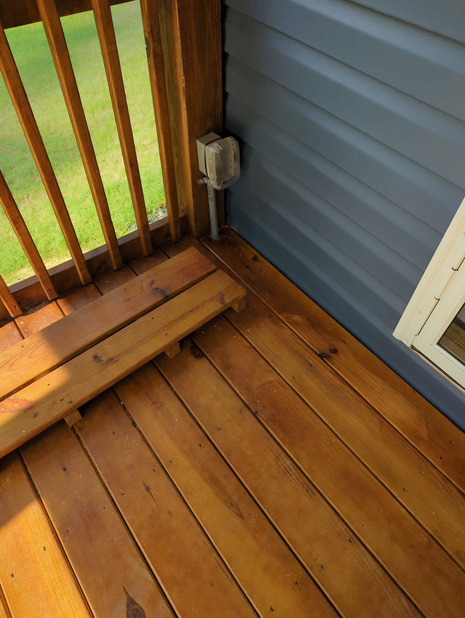 Wooden deck corner with railing, blue siding, and an electrical outlet near the floor.