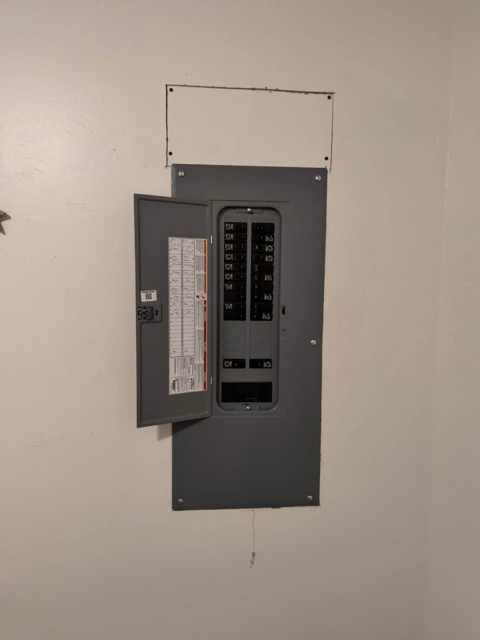 Open gray electrical breaker panel in a white wall, with the door ajar.