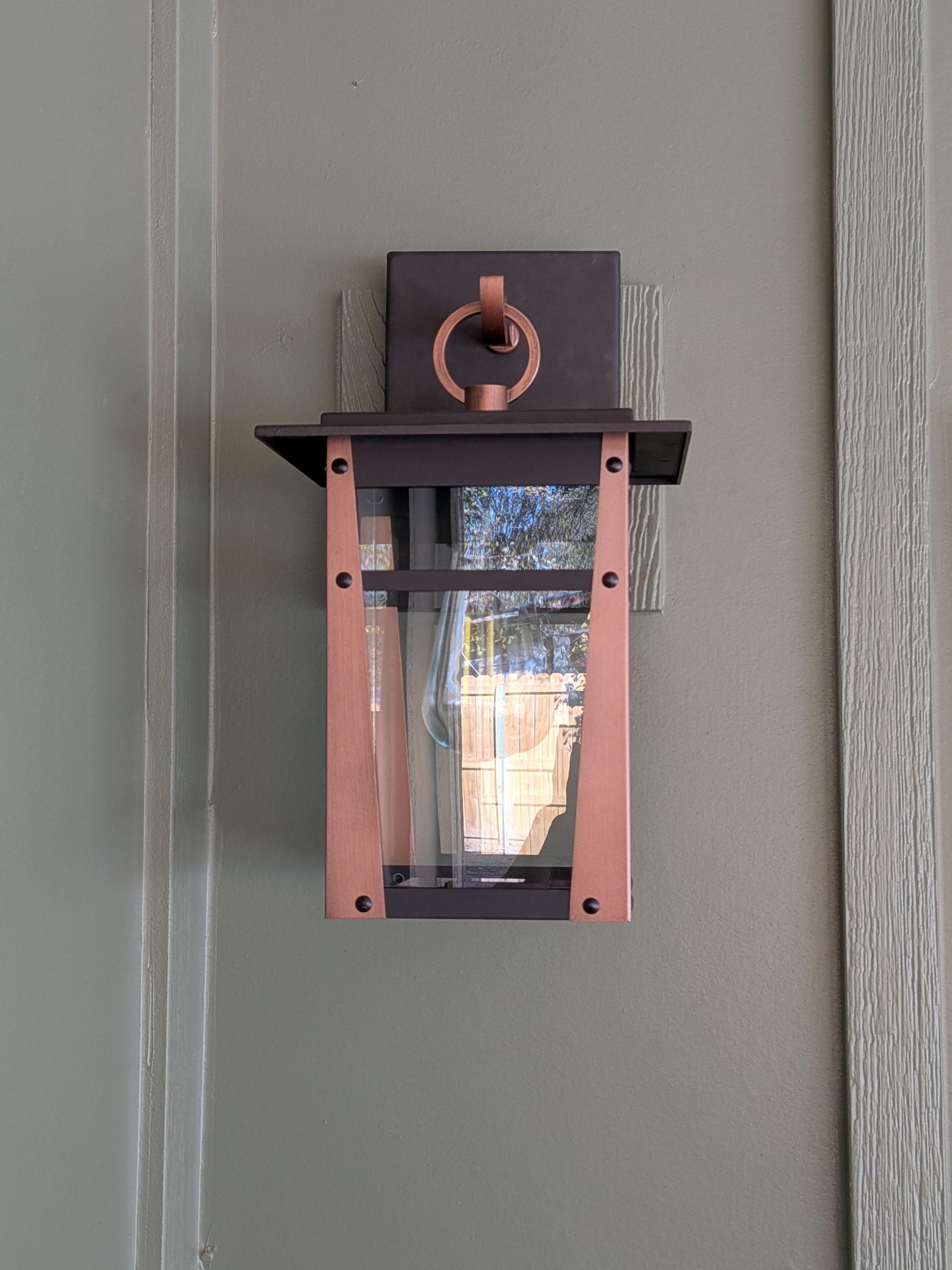 Rust-colored wall lantern on a gray exterior wall with a small shelf above it.