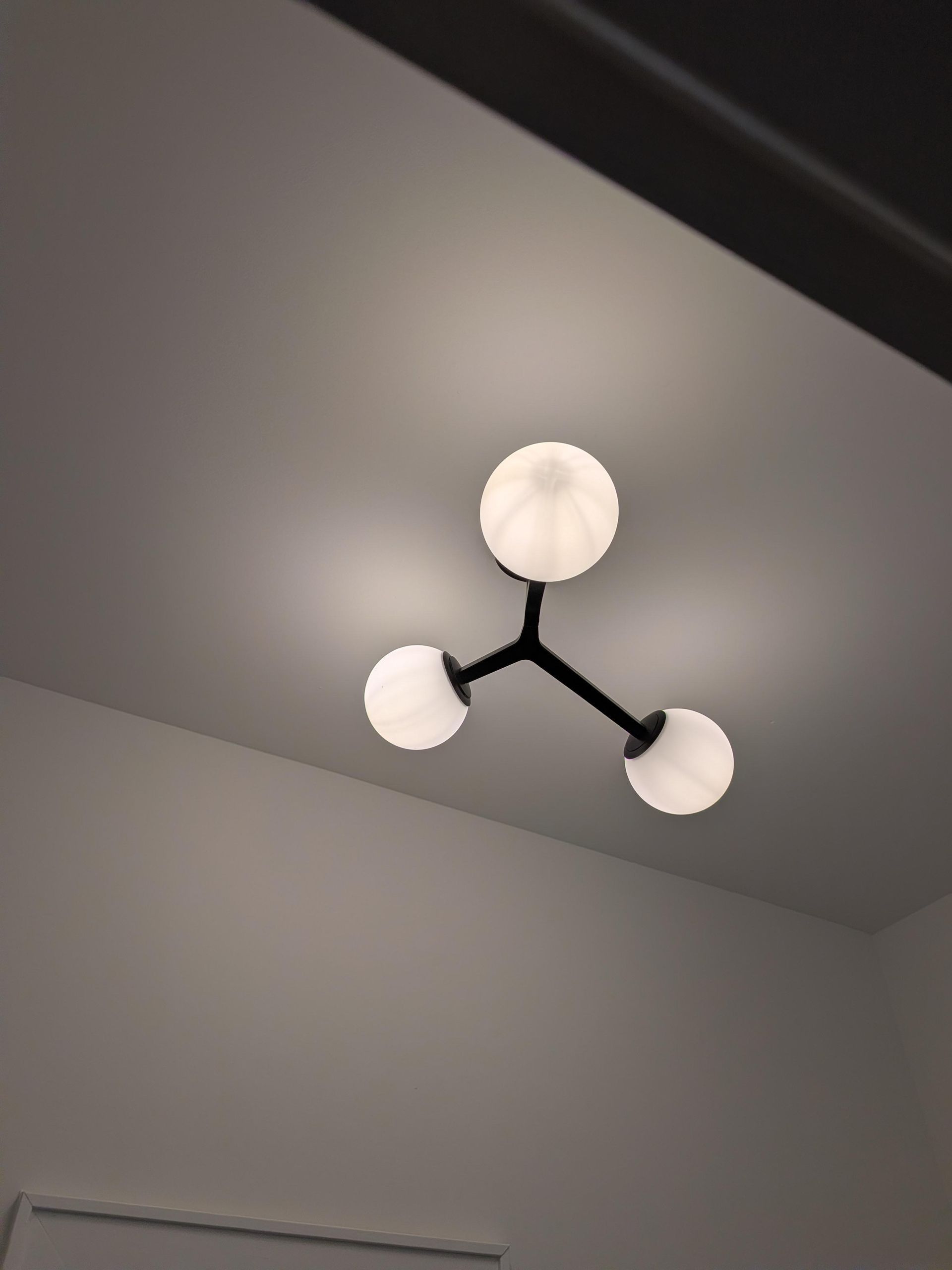 Modern ceiling light fixture with three white round shades on a gray ceiling