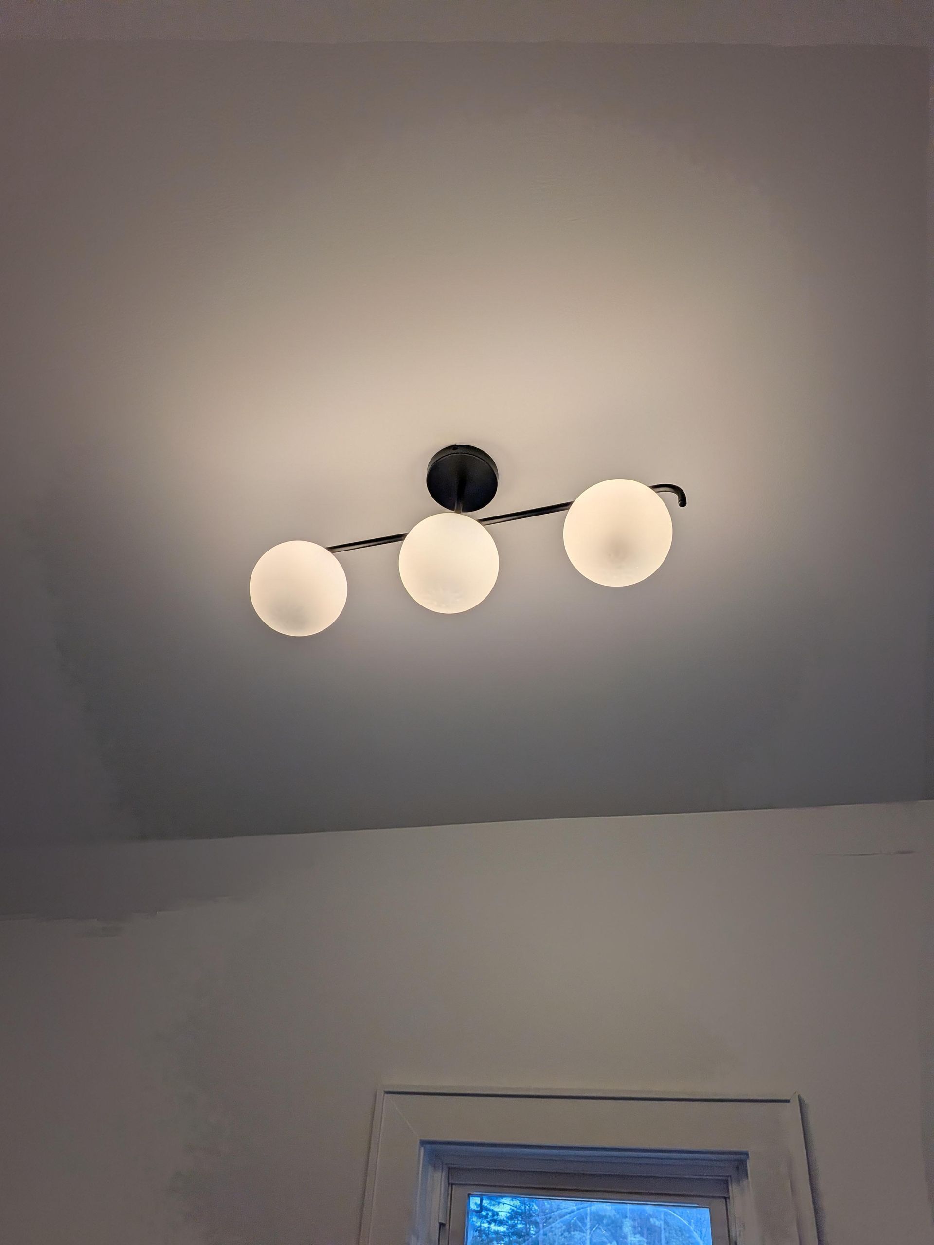 Ceiling light with three frosted globe bulbs above a doorway in a white room