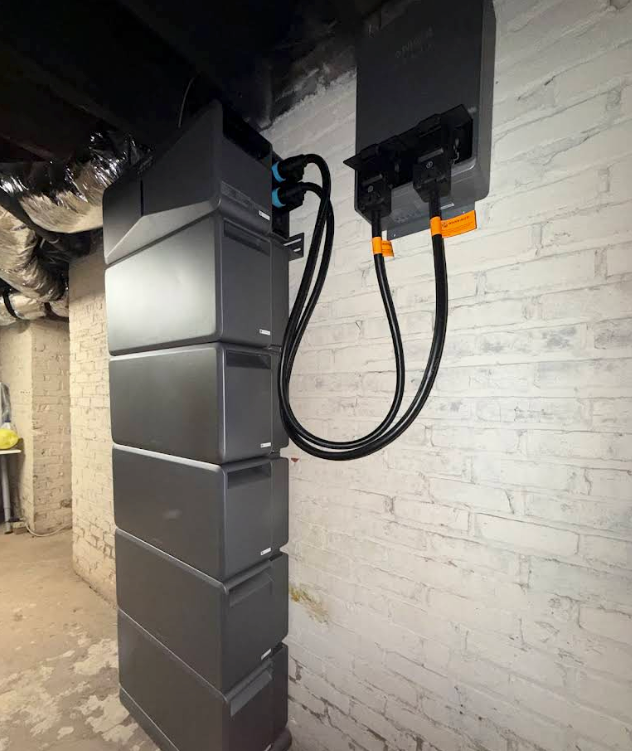 Basement electrical installation with gray ductwork and black control boxes mounted on a white brick wall