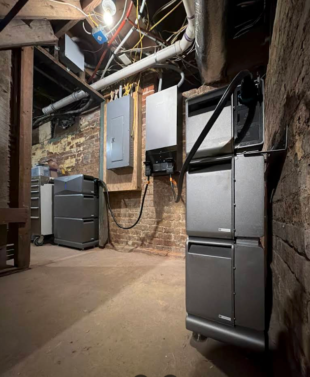 Basement utility room with furnace, electrical panels, and exposed pipes along brick walls.