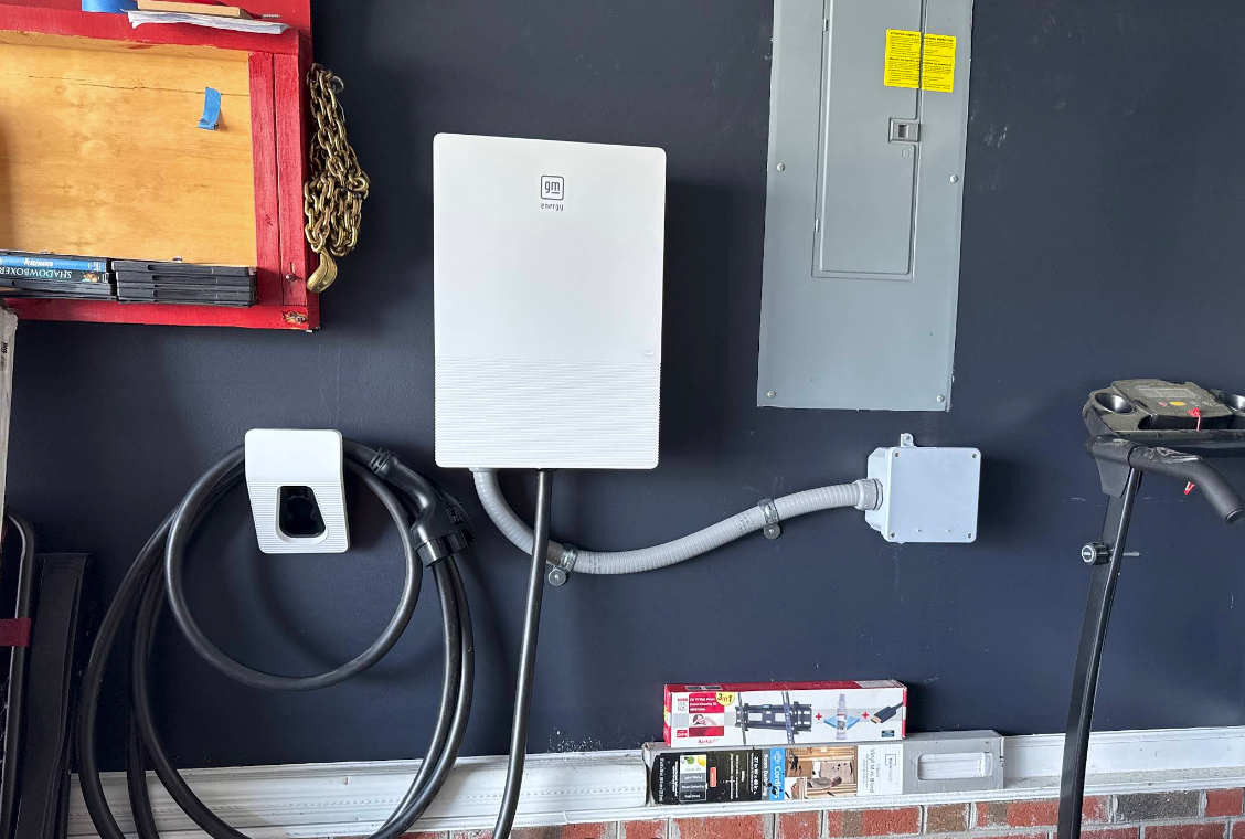 Wall-mounted electrical setup with gray panel, white box, cables, and outlets on a dark wall