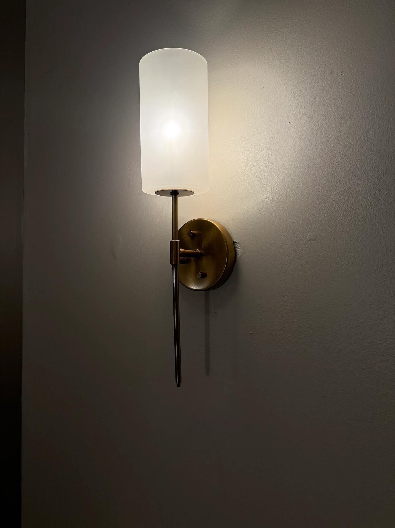Brass wall sconce with a frosted white glass shade casting soft light on a gray wall
