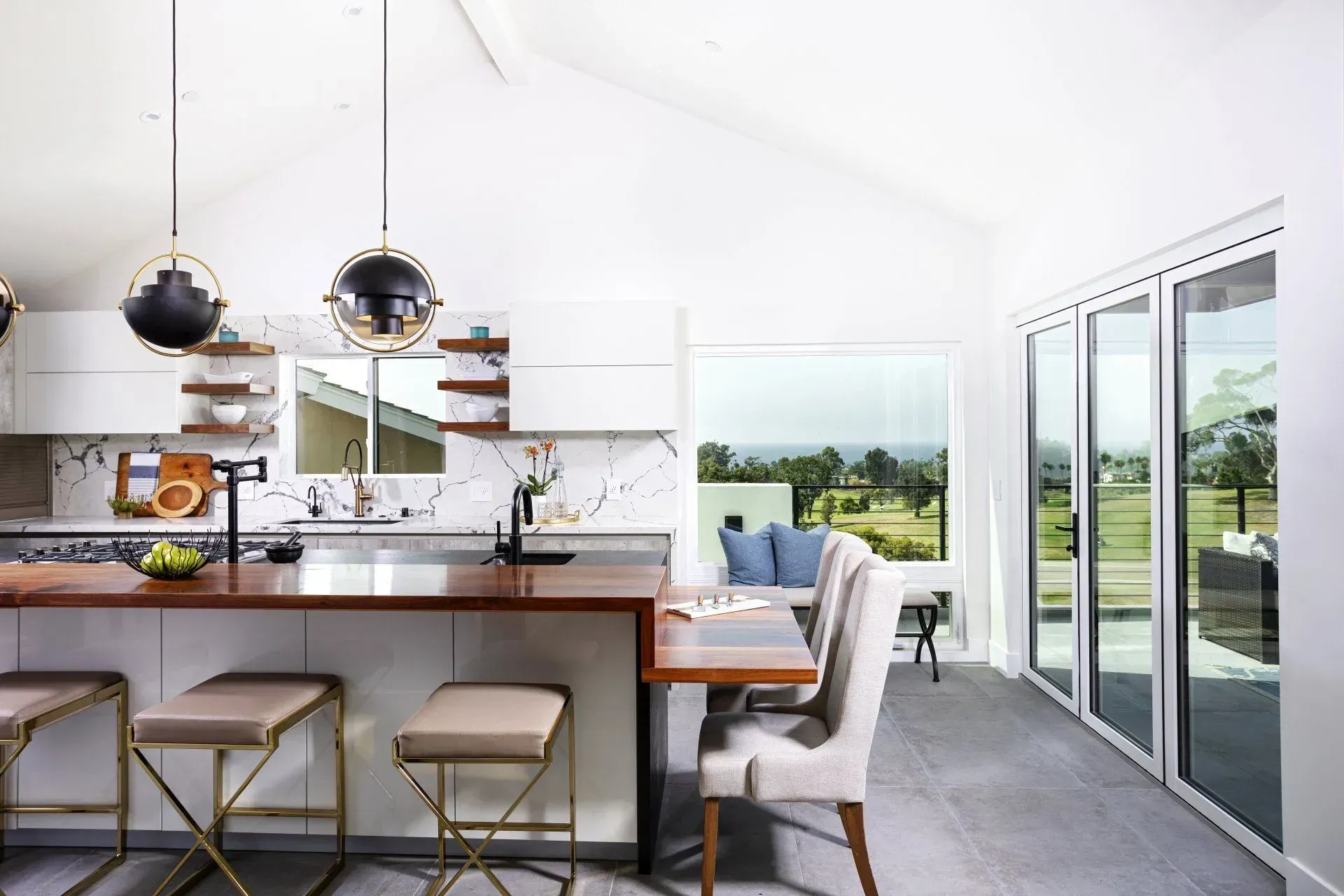 Modern kitchen with island, bar stools, table, window, and pendant lights.