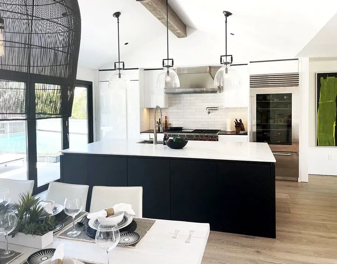Modern kitchen with black and white island, overhead lights, and dining table with place settings.