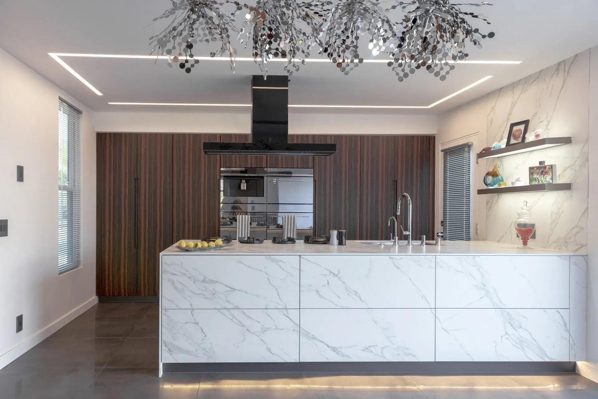 Modern kitchen with marble island, dark wood cabinets, and a reflective chandelier.
