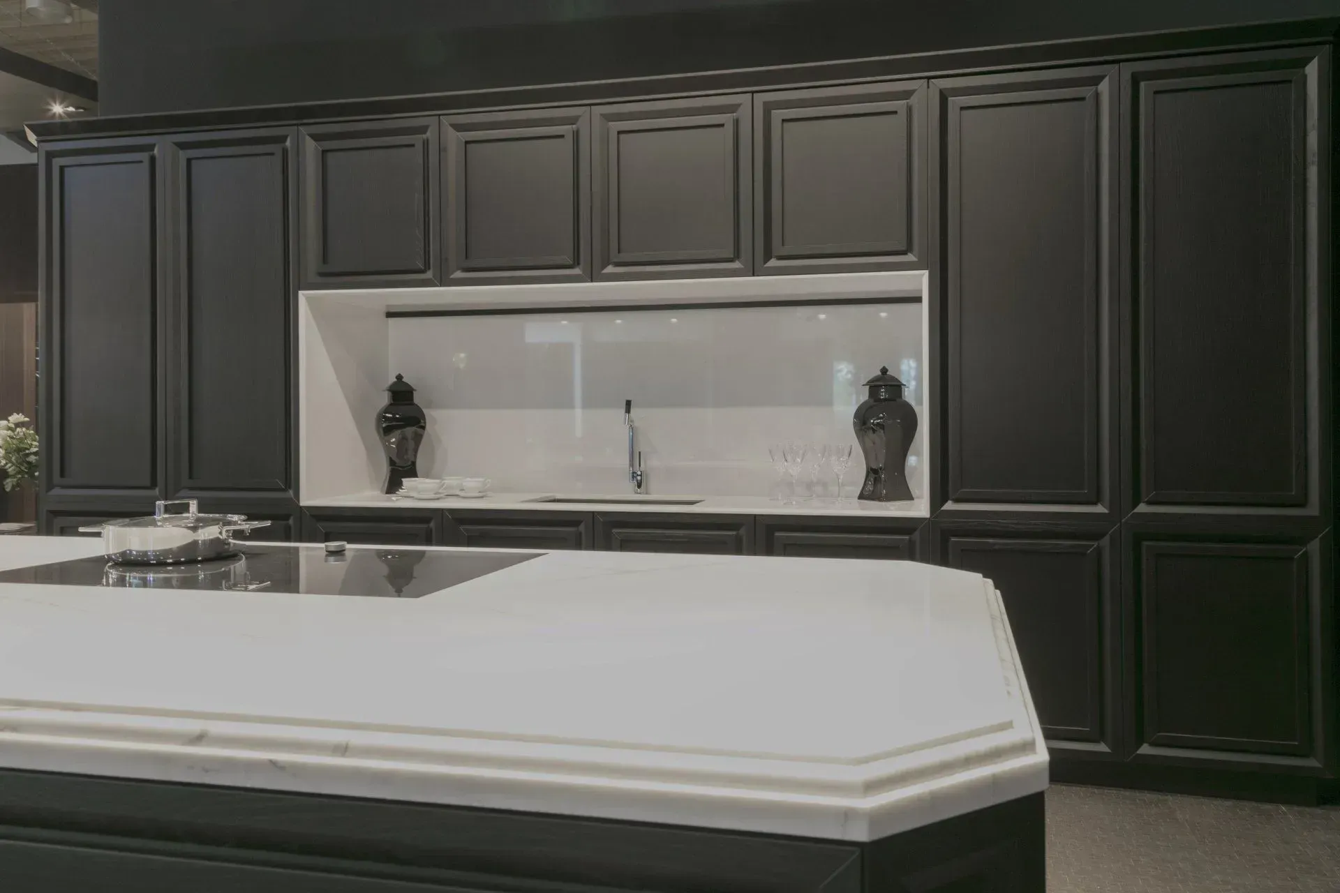 Black kitchen cabinets with white countertops and backsplash, island in the foreground.