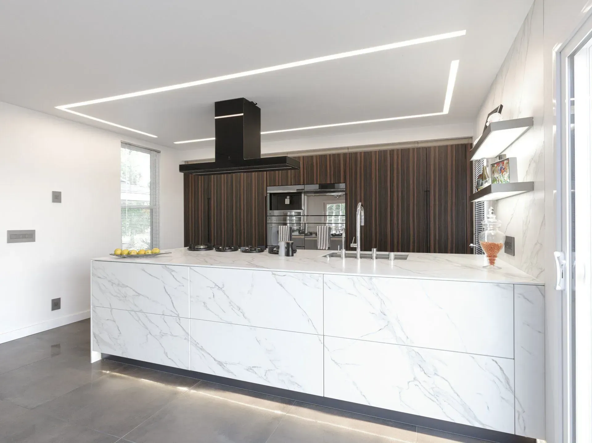 Modern kitchen with marble island, dark wood cabinets, and linear ceiling lights.