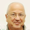 גבר קירח עם משקפיים מחייך למצלמה. הוא לובש חולצה אפורה על רקע בהיר.