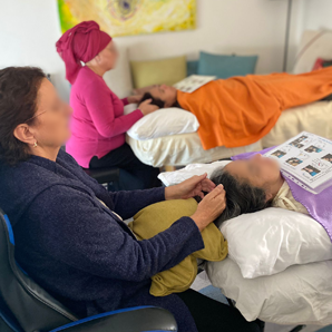 שלושה אנשים מקבלים עיסויי ראש בתוך הבית. שתי נשים בלבוש ורוד וכחול מעניקות טיפולים.