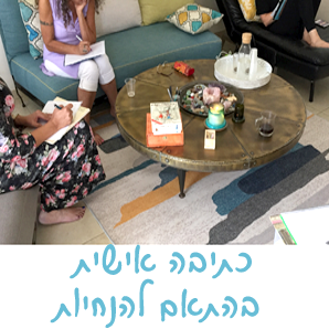 שלוש נשים כותבות במחברות בסלון. שולחן קפה עם חטיפים. טקסט בעברית בתחתית.