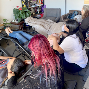 אנשים מקבלים עיסויי ראש בחדר. מספר מטפלים מעסים לקוחות, חלקם יושבים בכורסאות נוח. ניתן לראות שיער בצבעים בהירים.