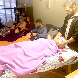 אנשים מקבלים טיפולי ראש וגוף על מיטות עיסוי בחדר מואר. מטפלים עובדים על כל לקוח.