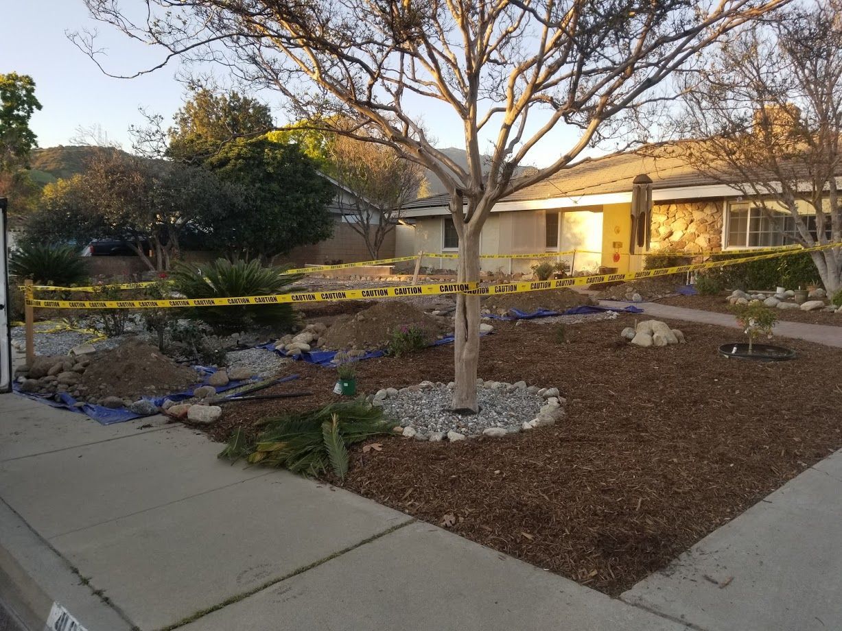 Front yard with landscaping under construction, yellow caution tape, tree, house in background.