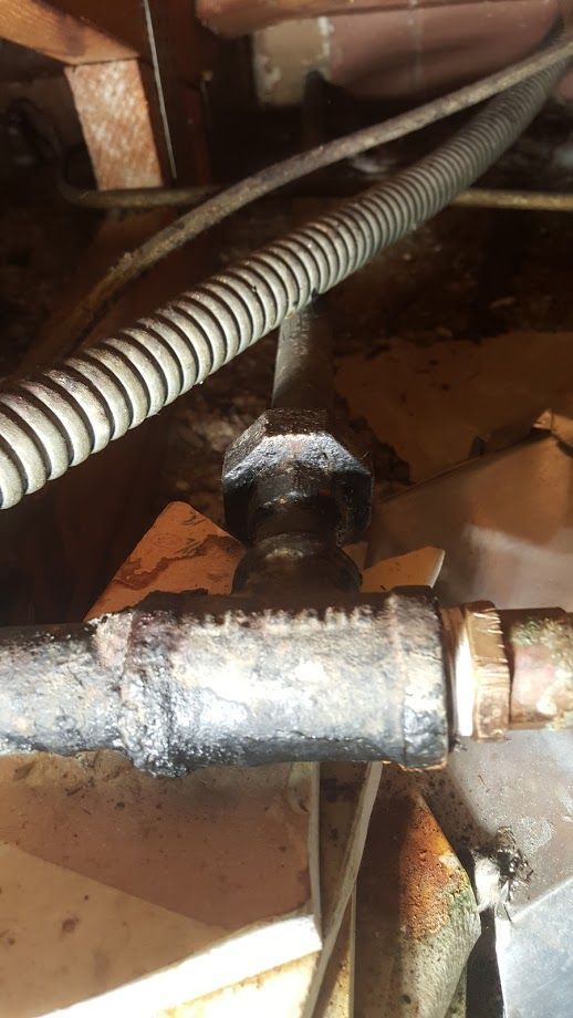 Black pipe joint with hexagonal head, flexible conduit, and wood beams in a dim setting.