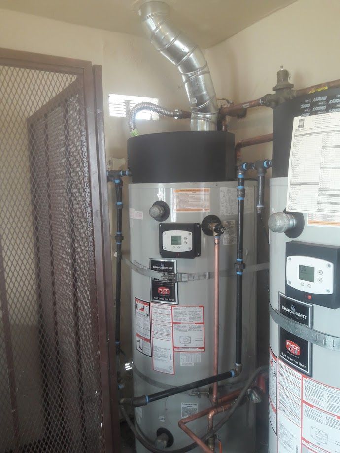 Two water heaters in a utility room with metal vent and pipes, digital control panels, and a metal security gate.