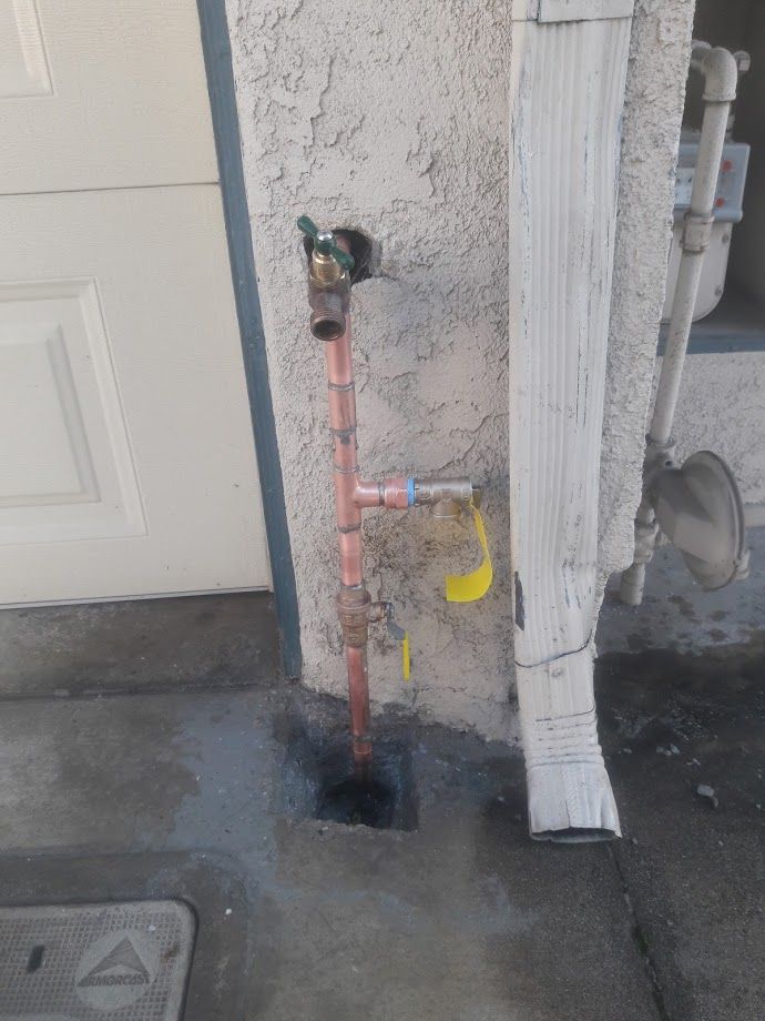Copper plumbing pipe with a faucet, near a white building wall and a gutter.