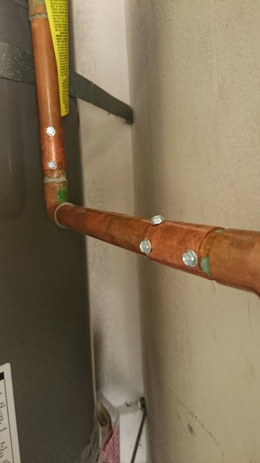 Copper pipes joined by metal fasteners near a wall and a water heater.