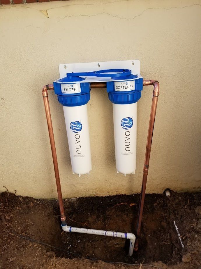 Two white Nuvo water filters with blue tops, mounted on a wall with copper pipes.