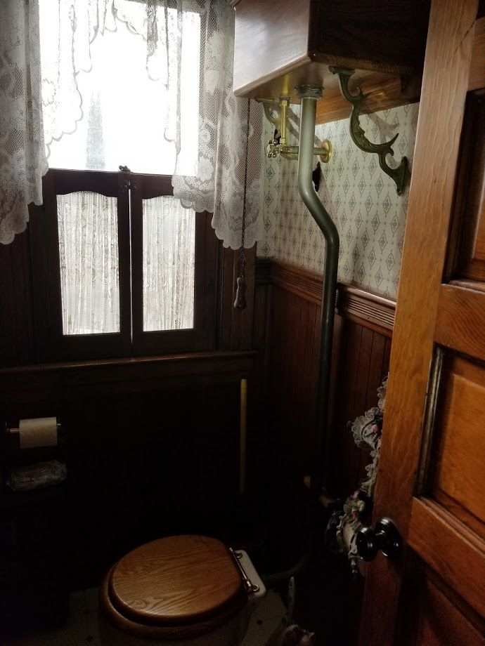 Bathroom with a toilet, wood paneling, lace curtains, and ornate fixtures.