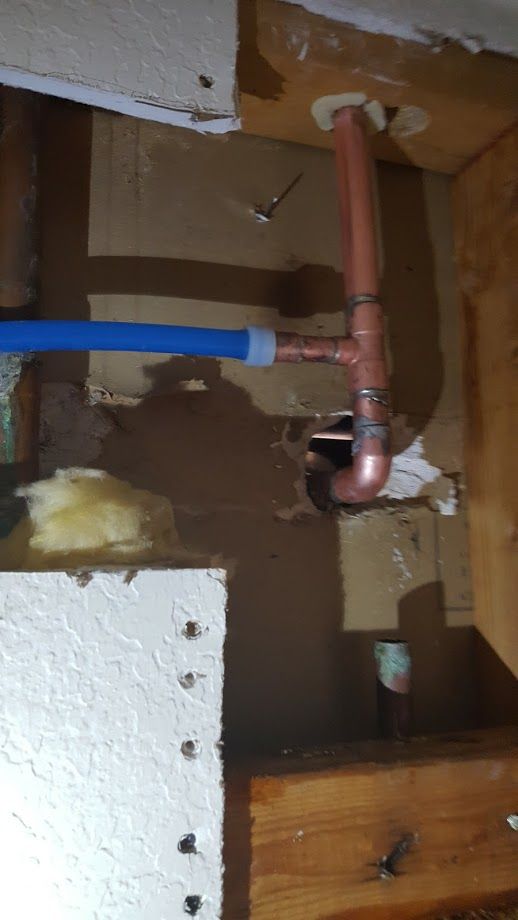 Copper plumbing pipes and blue PEX pipe against damaged wooden wall.