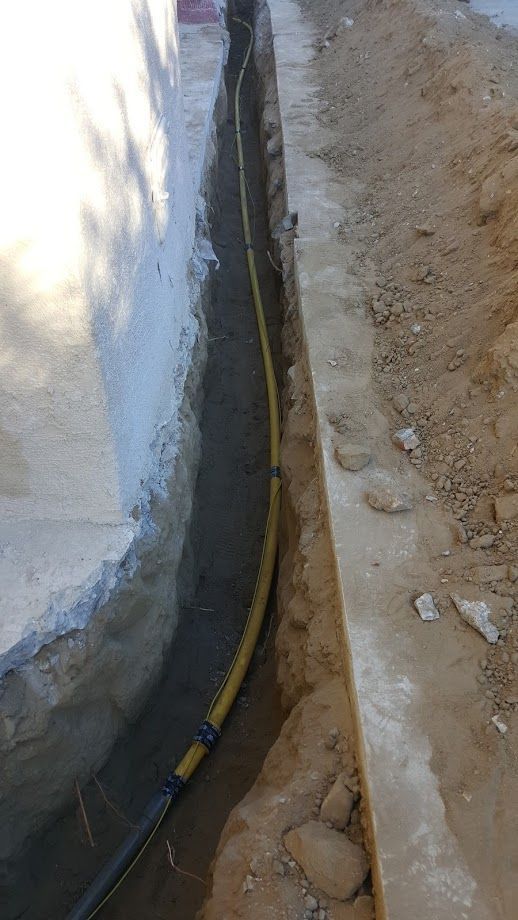 A trench with a yellow gas line running along a concrete wall.