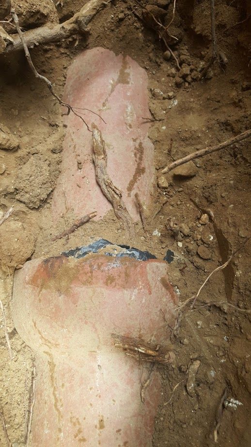 Broken clay pipe in a dirt trench, showing a section of the pipe, with cracks and earth around it.