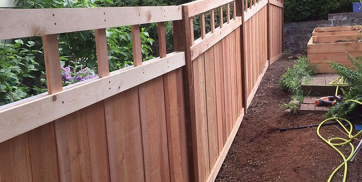 A newly installed redwood fence with a lattice-style top section, set in a garden with dark mulch and green plants.