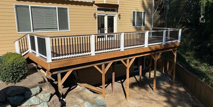 A wooden deck with a white railing and black balusters attached to the back of a tan house.