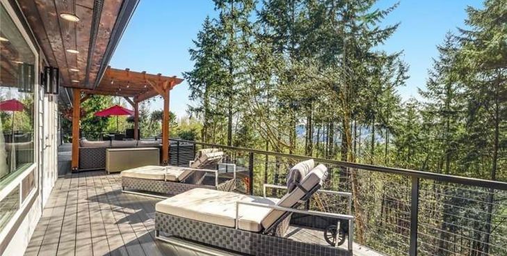 Two lounge chairs sit on a paved patio overlooking a forested hillside under a clear blue sky.