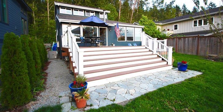 A dark blue house with a wide, multi-step wooden deck leading down to a stone patio and green lawn.