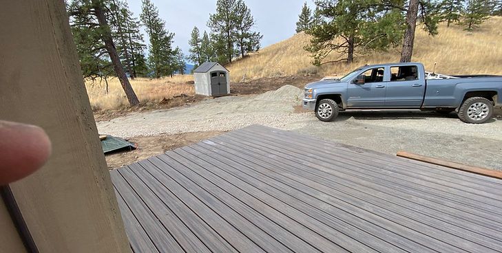 A grey pickup truck parked on a gravel driveway next to a small outdoor shed, viewed from a wooden deck.