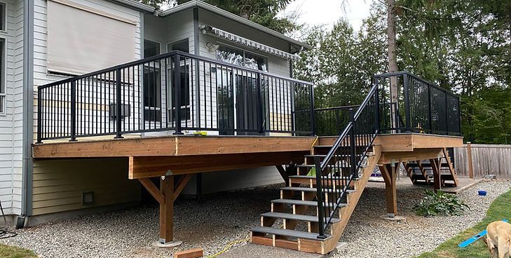 A raised wooden deck with black railings and stairs leading down to a gravel yard next to a house.
