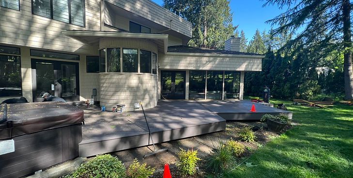 A multi-level composite deck extends from a light-colored home with a large curved window, set in a sunny backyard.
