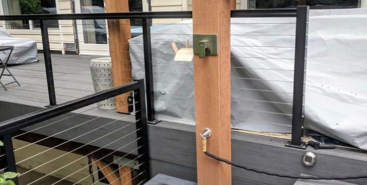 A close-up of a wooden deck post with a mounted outdoor electrical outlet and a plugged-in black power cord.