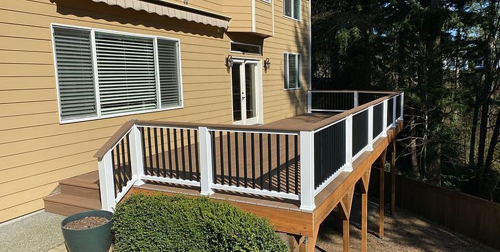 A wooden deck with a white railing and black balusters attached to the back of a tan house.