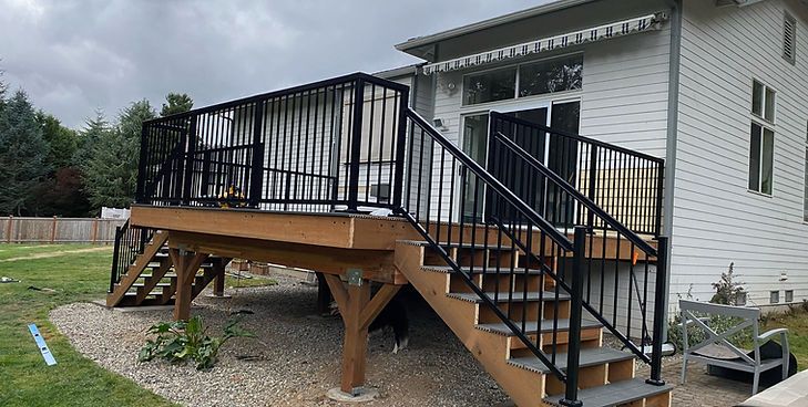 A wooden deck with black metal railings and stairs, attached to the back of a white house with a gravel yard.