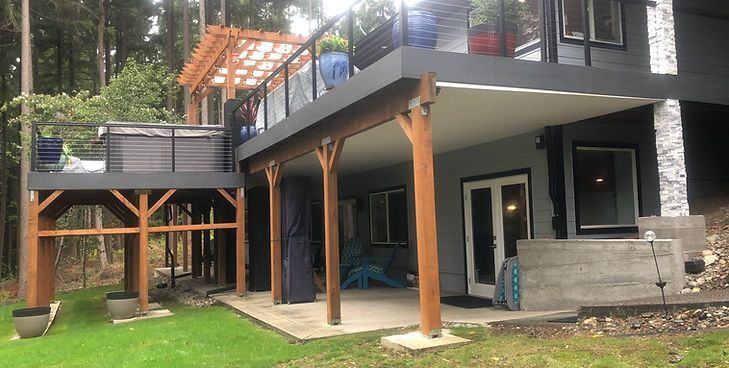 A two-story home exterior features a large wooden deck with a hot tub, a pergola, and a covered ground-level patio.