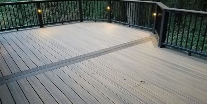 An elevated wooden deck with light gray planks, a dark brown accent border, and a black metal railing with integrated lights.