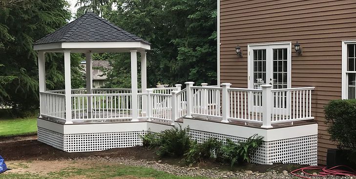 A white deck featuring a gazebo with a dark shingled roof attached to the side of a house with brown horizontal siding.