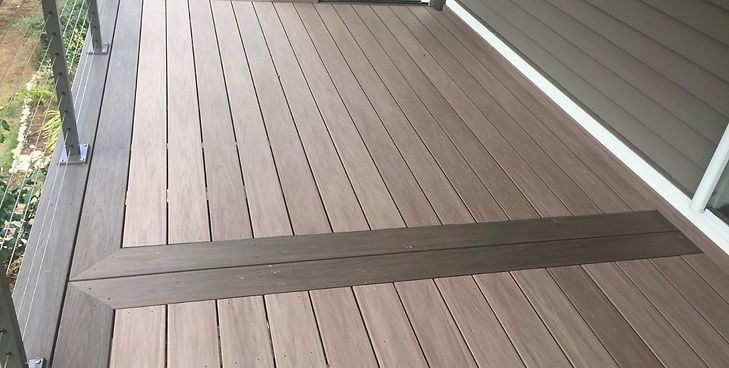 A modern outdoor deck with two-toned brown composite planks laid in a border pattern alongside a house.