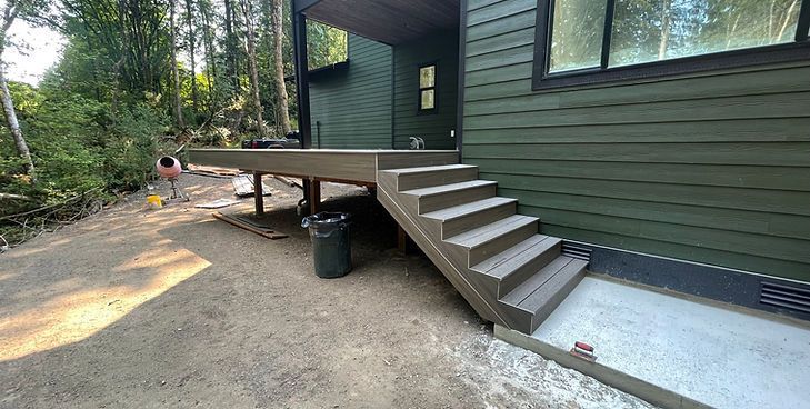A side view of a modern green house with a newly constructed elevated composite deck and a matching set of stairs.