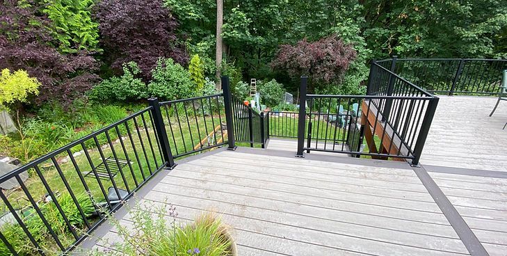 A composite deck featuring black metal railings and stairs leading down into a lush green backyard garden.